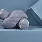 Die KraftKids GmbH Wickeltischrolle Waffel Piqué grau - ein strukturiertes, graues Kissen mit weißer Paspel - liegt auf einer blauen Fläche vor einem geometrischen blauen Hintergrund und eignet sich perfekt als Lagerkissen.