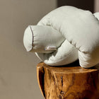 Eine leicht grünlich-weiße Wickeltischrolle Leinen von KraftKids GmbH sitzt geknotet auf einem polierten Holzhocker vor einer beigen Wand. Das Sonnenlicht beleuchtet die Rolle teilweise und wirft einen Schatten an die Wand.