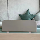 Ein minimalistisches Kinderbett mit einem grauen Kopfteil, hellem Bettzeug und zwei meergrünen Sternenkissen steht vor einer Betonwand und ist mit dem KraftKids Bettschutzgitter Rausfallschutz - grau ausgestattet, das für zusätzliche Sicherheit sorgt und leicht verstellbar ist.