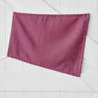 Eine einfarbig magenta-dunkle dreieckige Fahne von KraftKids, der Sonnensegel Leinen magenta dunkel, ist an eine weiße Holzwand mit diagonalen und vertikalen Paneelen gepinnt.