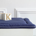 Ein Holzblock mit dem Buchstaben K ruht auf einer ordentlich gefalteten KraftKids Wickelauflage Leinen blau dunkelblau vor einer weißen Wand mit Zierleisten.