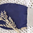 Der Strampelsack Frühling Sommer Leinen blau dunkelblau von KraftKids ruht auf einer dicken weißen Strickdecke, die mit getrocknetem beigem Laub bestückt ist.