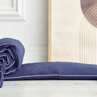 Eine dunkelblaue KraftKids Bettumrandung Nestchen Leinen mit weißer Paspel ist an einem Ende aufgerollt und liegt auf einem hellen Holzboden neben einem gerahmten abstrakten Kunstwerk.