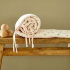 Eine gefaltete und gerollte KraftKids Bettumrandung Nestchen Musselin gelbe Zitronen mit einem kleinen Zitronenaufdruck sitzt auf einer Holzbank neben Holzkugeln, die an einer beigen Wand angebracht sind - perfekt für Ihr Babybett.