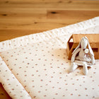 Eine kuschelige KraftKids Krabbeldecke Musselin Kirschen liegt auf einem Holzboden. Auf der Matte aus weichem Polyestervlies liegen ein Holzspielzeug-Bus und eine Stoffhasenpuppe in einem Kleid.