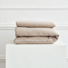 Das KraftKids Bettwäscheset Musselin beige aus 100 % Baumwolle ist ordentlich gefaltet und steht auf einem weißen Sockel vor einer weißen Wand mit Zierleiste.