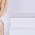 Eine hohe Korbvase mit beigem Pampasgras steht neben einer weißen, minimalistischen Bank, auf der die KraftKids GmbH Sitzauflage für Ikea TROFAST Musselin grau Pusteblumen steht. Der Hintergrund ist einfarbig weiß.