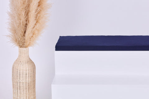 Eine hohe, geflochtene Vase mit hellbeigem Pampasgras steht neben einer weißen Bank mit dem KraftKids GmbH Sitzauflage für Ikea STUVA/SMÅSTAD Musselin dunkelblau Kissen, alles auf einem schlichten weißen Hintergrund.