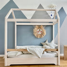 Ein minimalistisches Kinder-Holzhausbett mit KraftKids Bettwäscheset Leinen in hellgrün-weiß und Sternenkissen steht an einer blauen geometrischen Wand. Ein Strohlöwen-Wandbehang und ein Wolken-Mobile schaffen eine gemütliche Atmosphäre.