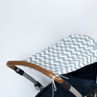 Eine Nahaufnahme zeigt ein KraftKids Sonnensegel Chevron hellgrau und mint auf einem Kinderwagen mit braunem Lenker, der auf weißem Hintergrund einen stilvollen Sonnenschutz für Kinderwagen bietet.