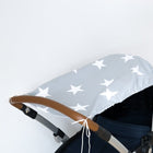 Der KraftKids Sonnensegel große weiße Sterne auf Grau, abgebildet auf einem Kinderwagen mit braunem Griff und grauem Verdeck mit großen weißen Sternen, bietet atmungsaktiven Baumwollsonnenschutz für Babys vor einem schlichten weißen Hintergrund.