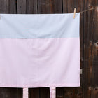 Der KraftKids Bezug für Wickeltischauflage kleine Blätter rosa auf Weiß aus 100% Baumwolle hängt an einer Wäscheleine vor einem Holzzaun. Der waschbare Bezug zeigt zwei rosa Bänder an der Unterkante.