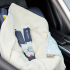 Eine KraftKids "Decke für Babyschale Winter weiße Diamante auf Pastell Blau" bedeckt einen Babyautositz auf der Rückbank eines Fahrzeugs. Die blau gemusterte Ecke, der Gurt und das Cybex-Etikett sind sichtbar, aber der Sitz ist leer.