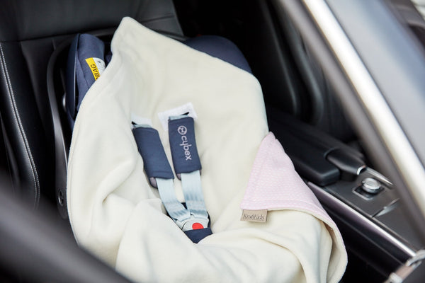 Eine KraftKids "Decke für Babyschale Winter kleine Blätter rosa auf Weiß" ist über einen auf dem Rücksitz eines Autos installierten Kindersitz drapiert. Der Gurt ist angelegt, und der Sitz scheint leer zu sein.