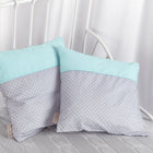 Zwei KraftKids Kissenbezüge "weiße Punkte auf Grau & Mint" liegen auf einer grauen Strickdecke und einem weißen Metallbett mit weißen Vorhängen - eine stilvolle Ergänzung für jede Bettwäschekollektion.