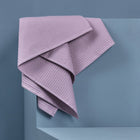 Die KraftKids Babydecke Waffel Piqué rosa aus weicher Baumwolle liegt über der Ecke einer blauen geometrischen Struktur vor blauem Hintergrund.