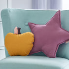 Ein hellblauer Sessel mit einem gelben apfelförmigen Kissen und einem KraftKids Sternkissen Musselin purpur auf der Sitzfläche, in einem sanft beleuchteten Kinderzimmer.