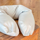 Ein beiger KraftKids Stillkissenbezug Leinen Natur Braun, weich und plüschig wie ein Leinen Stillkissen, liegt auf einer Holzbank mit einem Hartholzboden im Hintergrund.