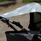 Eine Nahaufnahme eines grauen Kinderwagens mit dem KraftKids Sonnensegel große weiße Sterne auf Grau für optimalen Sonnenschutz, draußen im Sonnenlicht mit sichtbarer loser weißer Schnur.