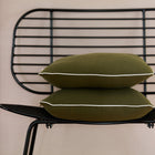 Zwei Kissenbezüge von KraftKids Kissenbezug Doppelkrepp Grün Herbstgrün sind auf einem modernen schwarzen Metallstuhl mit Drahtrückenlehne vor einer hellen Wand gestapelt.