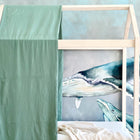 Eine KraftKids Bettbaldachin Doppelkrepp Grün Jade hängt über einem Holzbett vor einer blauen Wal-Wandmalerei. Eine beigefarbene Decke auf dem Bett fügt dem Unterwasser-Themenzimmer eine gemütliche Kinderzimmer Deko hinzu.