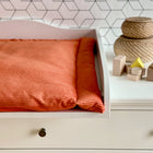 Ein weißer Wickeltisch mit einer KraftKids Wickelauflage Cord Breitcord Orange Reinorange, geflochtenen Körben und Holzspielzeugklötzen steht vor einer geometrisch gemusterten Wand.