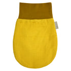 Der KraftKids Strampelsack Herbst Winter Waffel Piqué senf ist ein gelber, ovaler Babysack mit waffelartiger Oberfläche, einem glatten braunen Bündchen und einem kleinen Seitenanhänger.