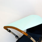 Nahaufnahme eines Kinderwagens mit einem mintfarbenen, mit weißen Punkten gemusterten Verdeck (KraftKids Sonnensegel weiße Punkte auf Mint) und einem braunen Griff aus Kunstleder vor einem schlichten weißen Hintergrund.