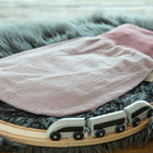 Ein KraftKids Strampelsack Herbst Winter Doppelkrepp Rosa in zartem Rosa und Mauve ruht auf einem flauschigen grauen Teppich, umgeben von einer hölzernen Spielzeugeisenbahn mit einem schwarz-weißen Zug.