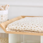 Eine Nahaufnahme der KraftKids Bezug für Wickeltischauflage Musselin Zweige braun zeigt die cremefarbene Farbe und das braune Zweigmuster, mit einem passenden Aufbewahrungsbehälter und einer Decke im Hintergrund. Hergestellt aus 100% Baumwolle.