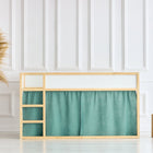 Ein minimalistisches Kinderzimmer mit einem hellen holzgerahmten IKEA Kura Hochbett, gestylt mit dem KraftKids Musselin nilblau Hochbettvorhänge Set 2+1, einem geflochtenen Korb mit Pampasgras auf der linken Seite und zwei Holzhockern vor einer weiß getäfelten Wand.