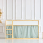 Ein minimalistisches IKEA Kura Hochbett mit hellem Holzrahmen, eingebauter Leiter und mintfarbenem Musselin Hochbettvorhänge Set 2+1 von KraftKids darunter, in einem weißen Kinderzimmer mit schlichter Wandverkleidung, Pampasgras in einem Korb und zwei Holzhockern.